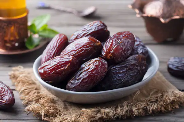 Dates in a white bowl on rustic cloth with herbal remedies background, highlighting natural health products and traditional remedies from Abbasi Herbal Corner.